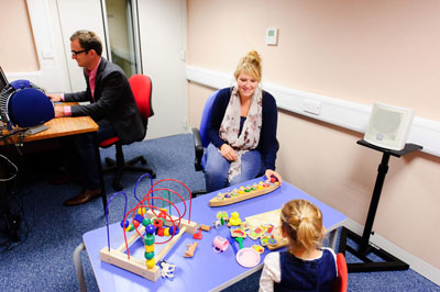 woman and man examine child's hearing in audiometric sound room
